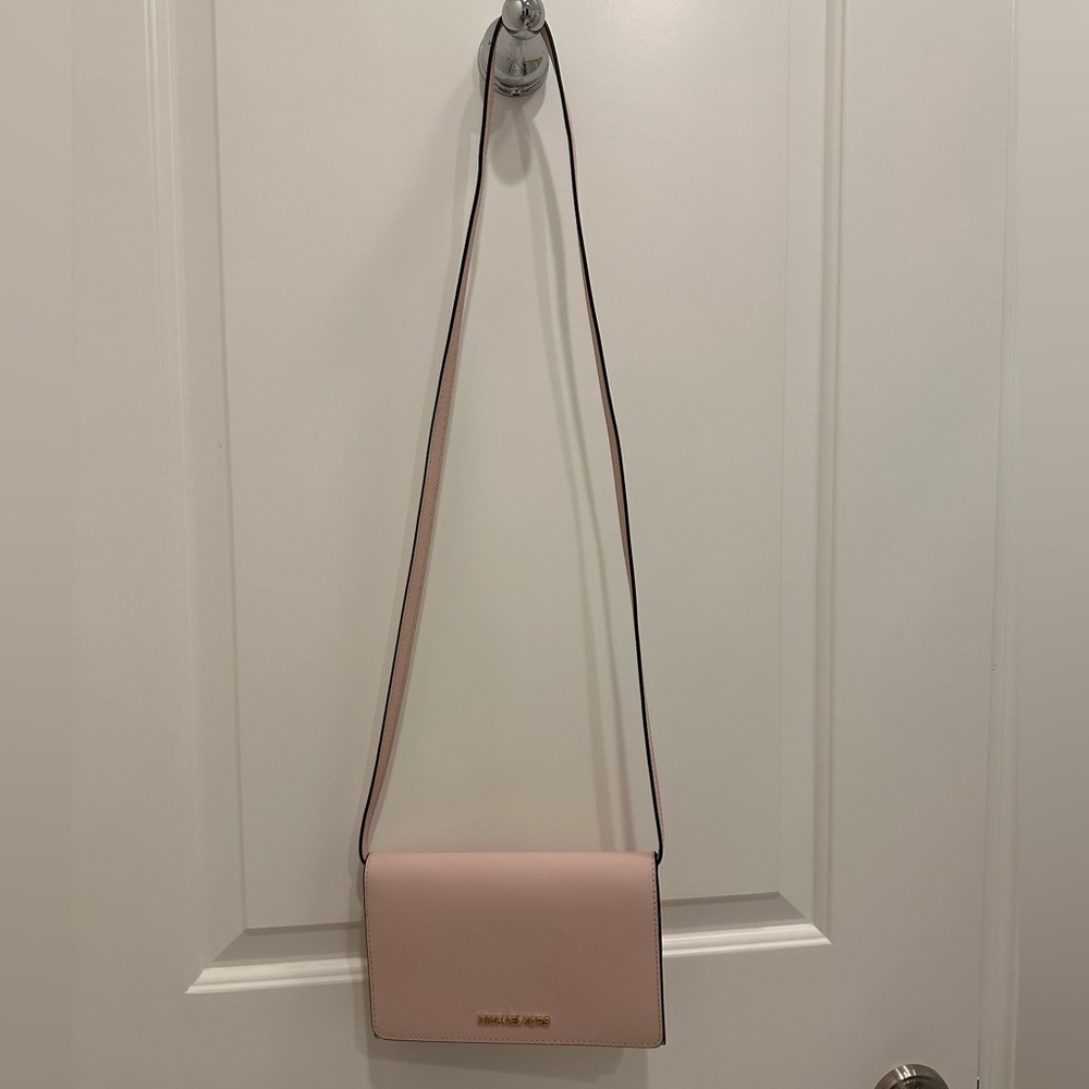 Small Light Pink Michael Kors purse with a strap.